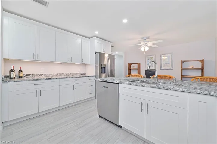 Kitchen with white cabinetry, sink, ceiling fan, light stone counters, and appliances with stainless steel finishes