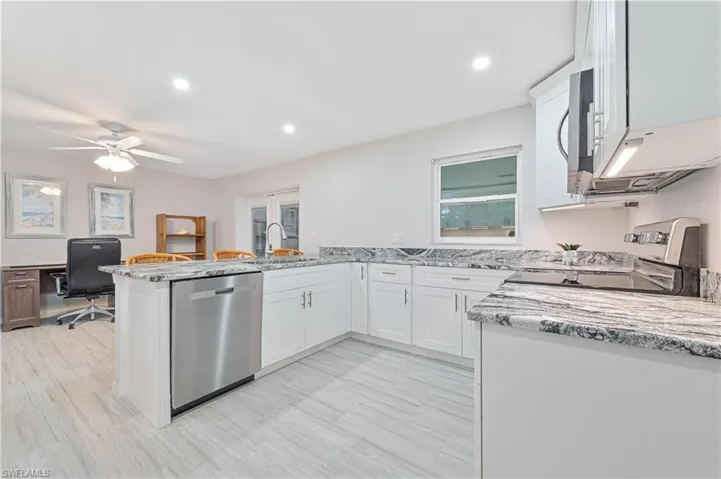 Kitchen with light stone countertops, sink, kitchen peninsula, white cabinets, and appliances with stainless steel finishes