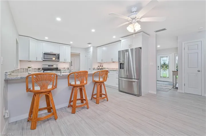 Kitchen featuring light stone countertops, kitchen peninsula, a breakfast bar area, white cabinets, and appliances with stainless steel finishes