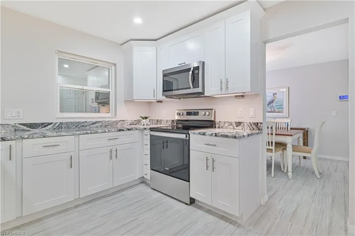 Kitchen with light hardwood / wood-style flooring, stainless steel appliances, white cabinetry, and light stone counters