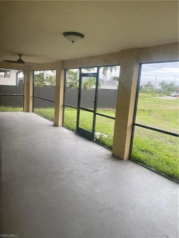 Spacious screened patio featuring a ceiling fan, flush-mount light fixture, textured columns, and a concrete floor