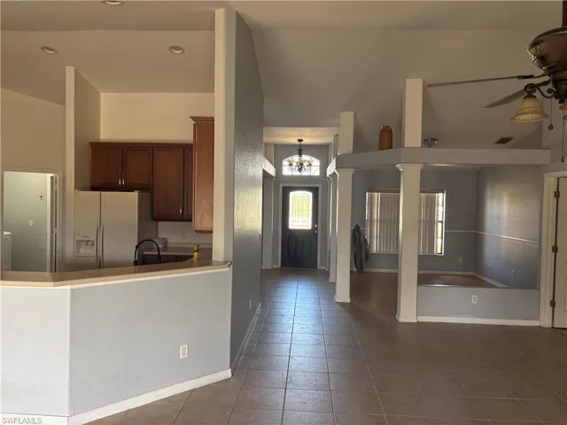 Kitchen with ceiling fan with notable chandelier, white fridge with ice dispenser, visible vents, tile patterned floors, and open floor plan