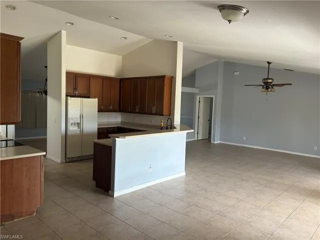 Kitchen featuring a peninsula, light tile patterned floors, white fridge with ice dispenser, open floor plan, and ceiling fan