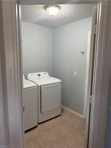 Washroom featuring laundry area, a textured ceiling, washing machine and clothes dryer, light tile patterned floors, and baseboards