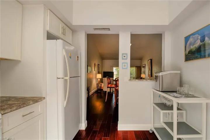 Kitchen featuring visible vents, white cabinets, freestanding refrigerator, and dark wood-style flooring