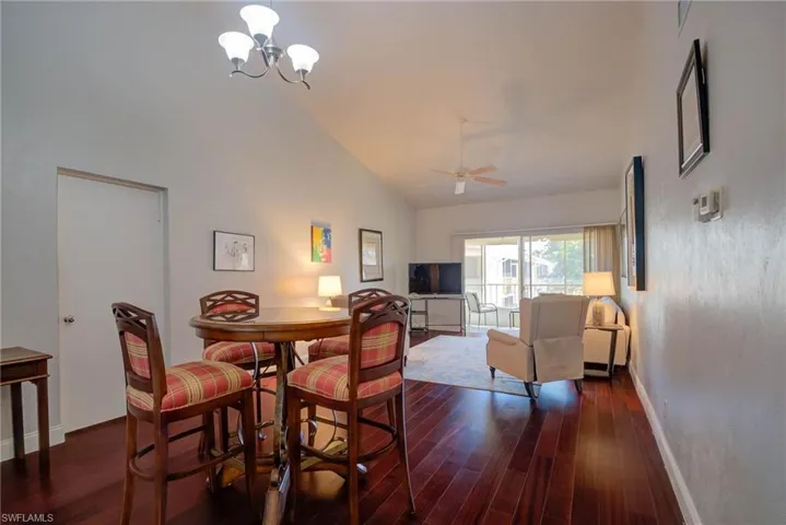 Dining area with ceiling fan with notable chandelier, high vaulted ceiling, dark wood-type flooring, and baseboards
