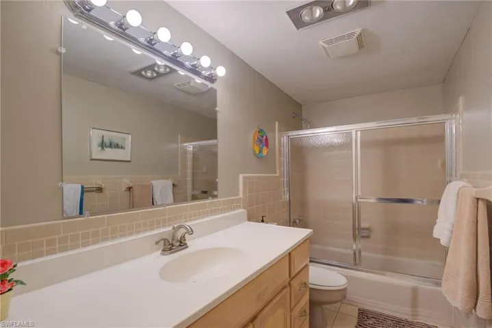 Bathroom featuring visible vents, bath / shower combo with glass door, toilet, vanity, and tile walls