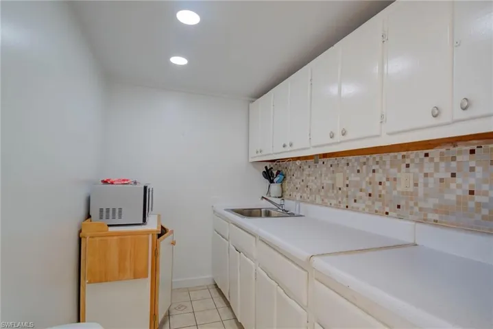 Clothes washing area featuring light tile patterned floors, recessed lighting, baseboards, and a sink