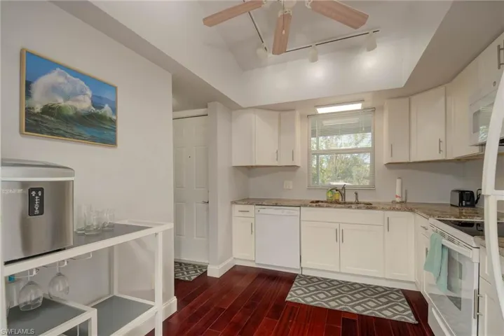 Kitchen with dark wood-type flooring, light stone counters, a sink, white appliances, and white cabinets