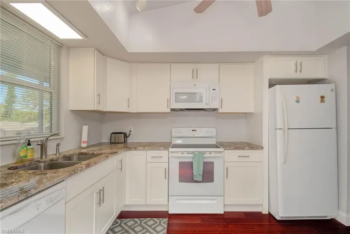 Kitchen with white cabinetry, white appliances, light stone countertops, and a sink