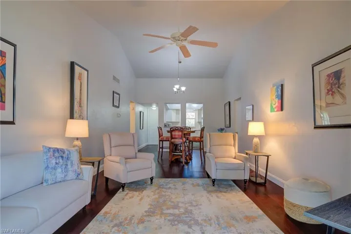 Living area with visible vents, high vaulted ceiling, ceiling fan with notable chandelier, wood finished floors, and baseboards