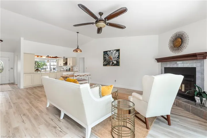 Living room featuring lofted ceiling, light wood-style floors, a ceiling fan, and a tiled fireplace