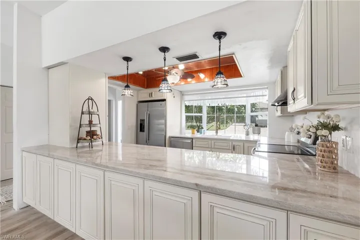 Kitchen with stainless steel appliances, light stone countertops, wall chimney exhaust hood, and pendant lighting