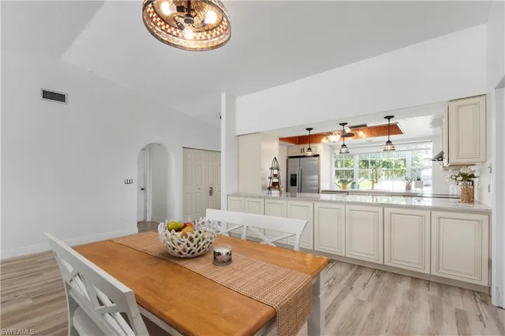 Dining area with light wood finished floors, lofted ceiling, arched walkways, and a chandelier