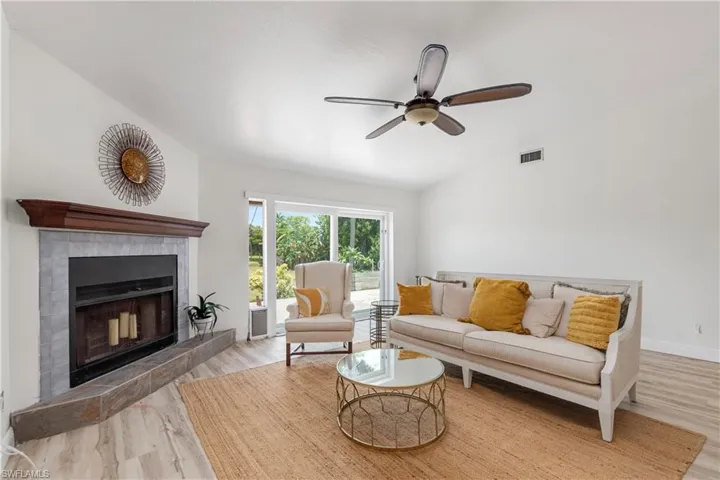 Living area with wood finished floors, vaulted ceiling, a fireplace, and a ceiling fan