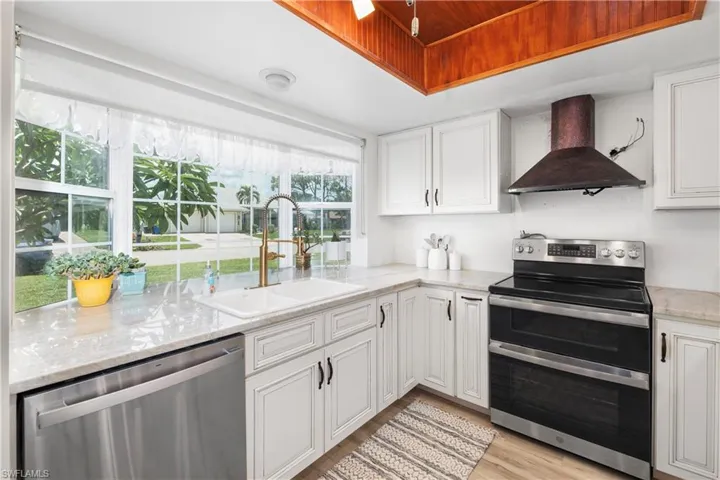 Kitchen featuring wall chimney exhaust hood, appliances with stainless steel finishes, white cabinets, light wood-style flooring, and light stone countertops