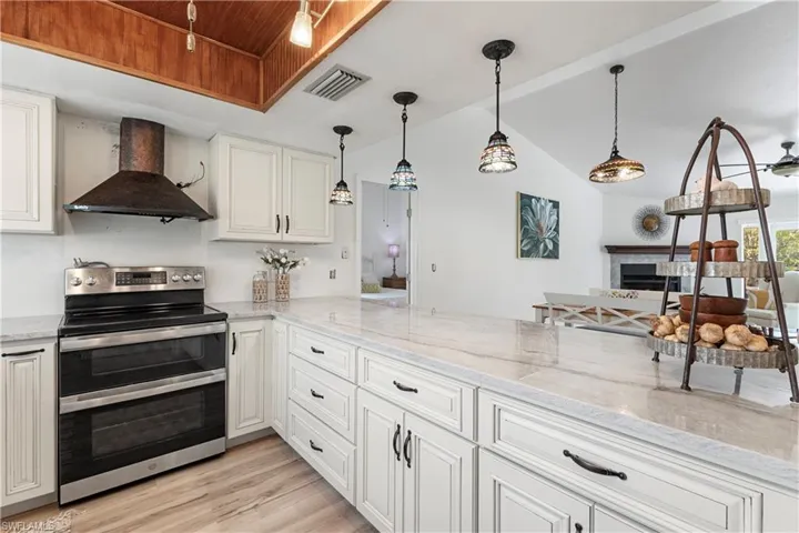 Kitchen featuring double oven range, wall chimney range hood, light wood-style flooring, a fireplace, and vaulted ceiling