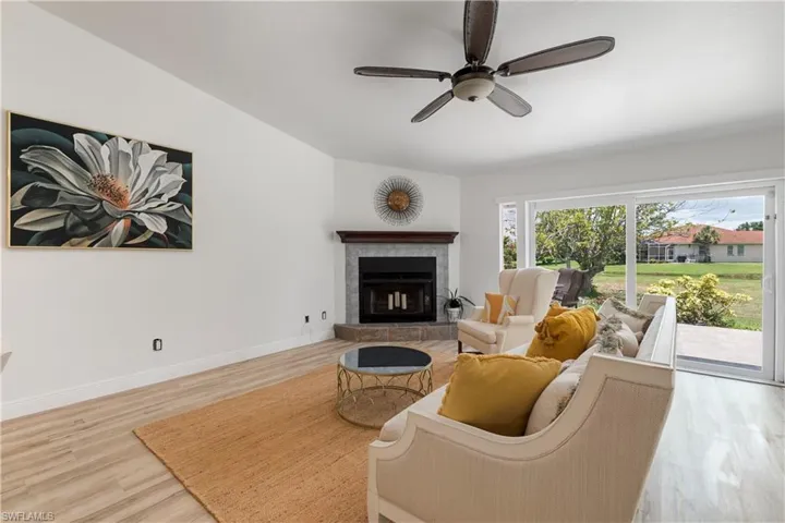 Living room featuring light wood finished floors, a ceiling fan, and a brick fireplace