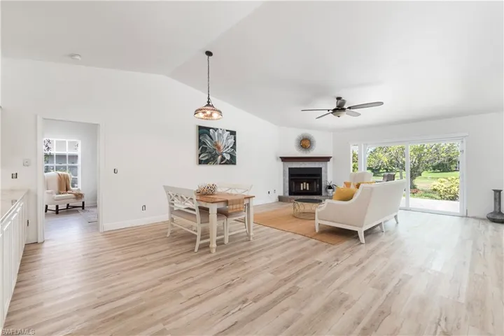 Living room featuring a ceiling fan, light wood finished floors, a fireplace with raised hearth, and vaulted ceiling