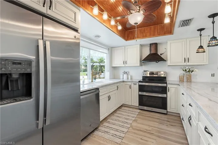 Kitchen featuring appliances with stainless steel finishes, wall chimney range hood, a ceiling fan, wood ceiling, and a tray ceiling