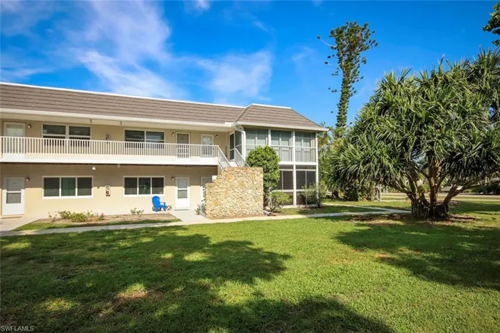 Two-story building exterior with a tiled roof, second-story balcony with white railing, stone staircase, and a screened-in porch