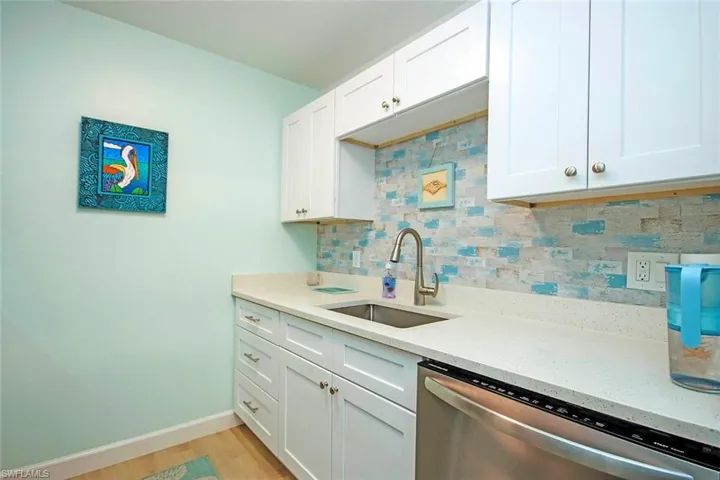 White shaker-style cabinetry, light-toned countertops, stainless steel sink with a gooseneck faucet, light wood-finish flooring, and a decorative tile backsplash