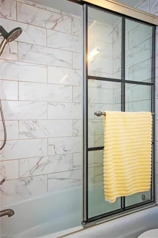 Subway tile shower surround with marble-look finish, full bathtub, and sliding glass shower doors