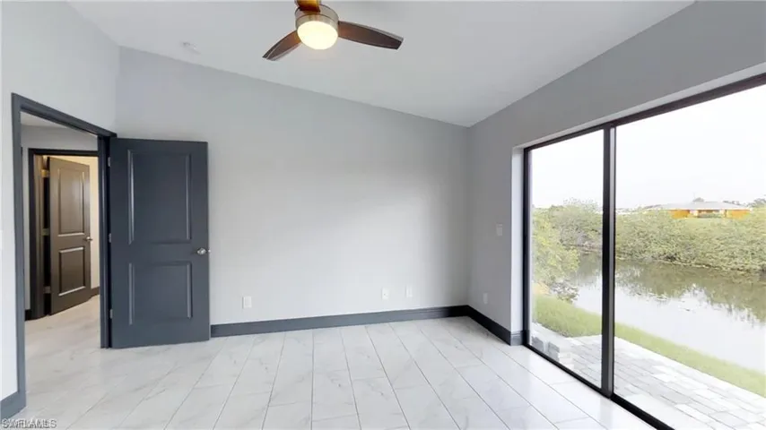 Vaulted ceiling, ceiling fan with integrated lighting, tile flooring, sliding glass door, and water frontage