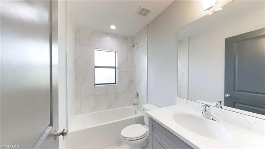 Bathroom featuring a white bathtub, tiled shower surround, frosted window, single vanity with an integrated sink, and a large wall mirror