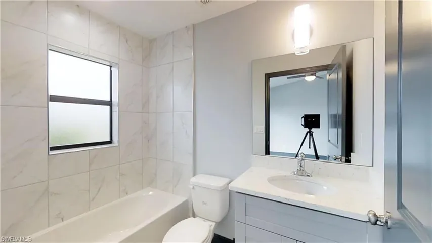 Bathtub and shower combination with full-height tile surround, single-basin vanity with a light-toned countertop, and a wall-mounted rectangular mirror