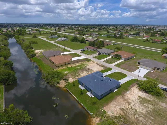 Waterfront property featuring a newly constructed residence with a dark shingle roof, concrete driveway, and established lawn
