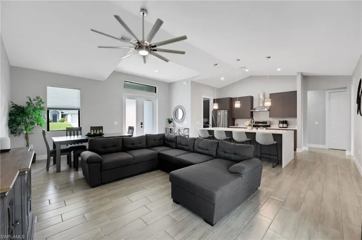 Spacious open-concept living area featuring wood-finish tile flooring, vaulted ceilings, and a modern ceiling fan