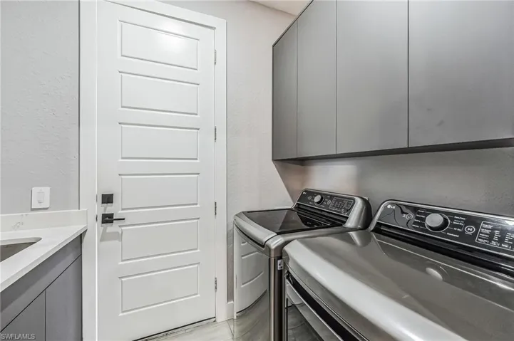 Laundry area featuring a built-in sink, stone countertop, matte gray cabinetry, and white paneled door