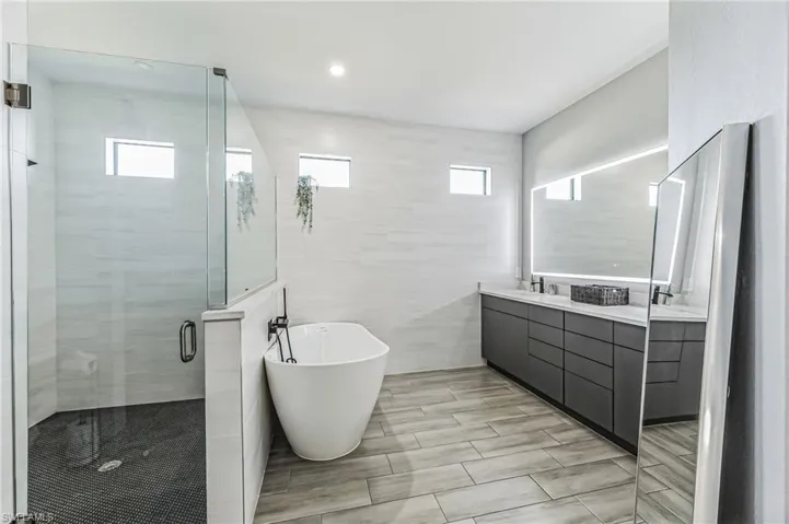 Modern bath featuring a frameless glass shower enclosure, a standalone soaking tub, and a dual vanity with a lighted mirror