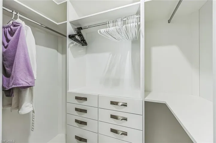 Custom white built-in closet system featuring multiple hanging rods, eight storage drawers with modern pulls, and integrated shelving