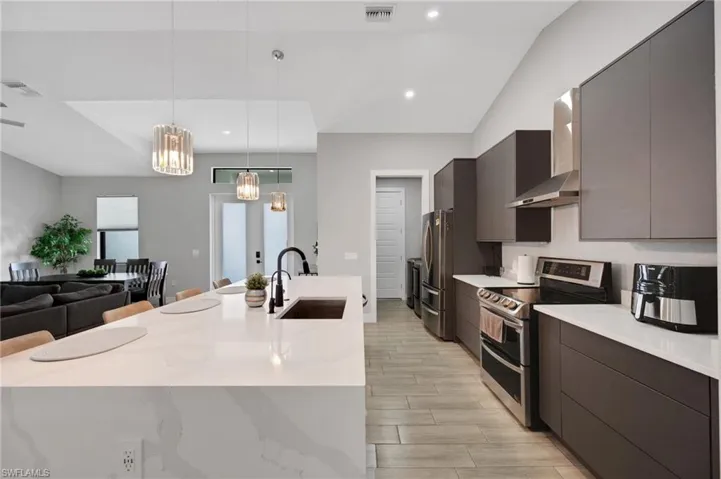 Modern kitchen featuring a waterfall-edge island with seating, stainless steel appliances, dark flat-panel cabinetry, and wood-finish flooring