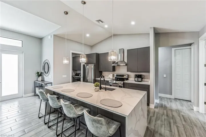 Gourmet kitchen featuring a large island with waterfall countertop, stainless steel appliances, dark gray cabinetry, and pendant lighting