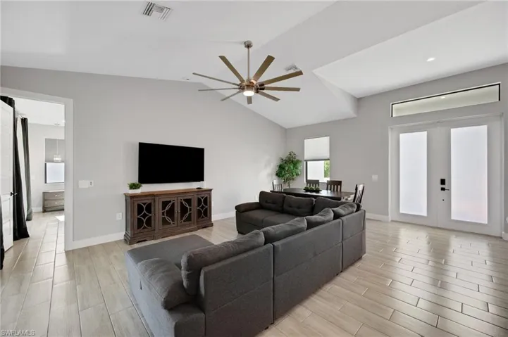 Open-concept living area with vaulted ceilings, large decorative ceiling fan, wood-finish tile flooring, double entry doors with transom window, and an integrated dining area