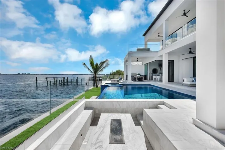 View of swimming pool with ceiling fan, a dock, a water view, and an outdoor fire pit