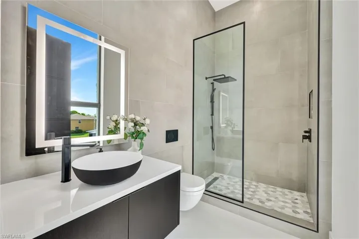 Bathroom with tile patterned floors, vanity, tiled shower, tile walls, and toilet