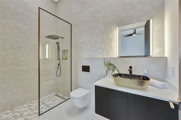 Bathroom featuring vanity, backsplash, toilet, tile walls, and a tile shower
