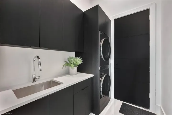 Clothes washing area with cabinets, sink, and stacked washing maching and dryer