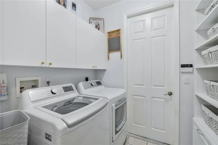 Laundry room with washing machine and clothes dryer, light tile patterned flooring, and cabinet space
