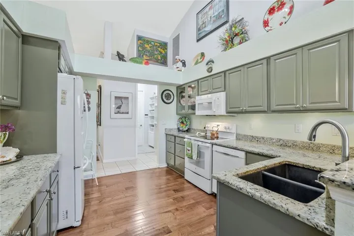 Kitchen featuring white appliances, light stone counters, light wood-style flooring, gray cabinets, and a towering ceiling