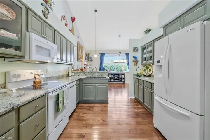 Kitchen with glass insert cabinets, white appliances, hanging light fixtures, a peninsula, and light stone countertops