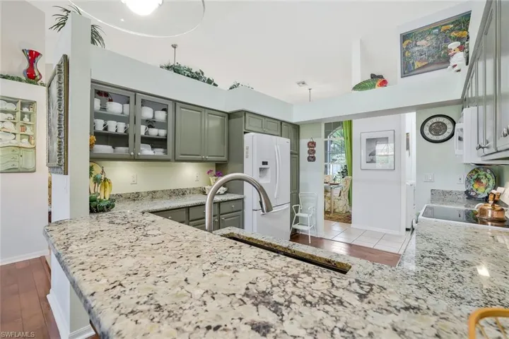 Kitchen featuring glass insert cabinets, white refrigerator with ice dispenser, range with electric stovetop, light stone counters, and gray cabinetry