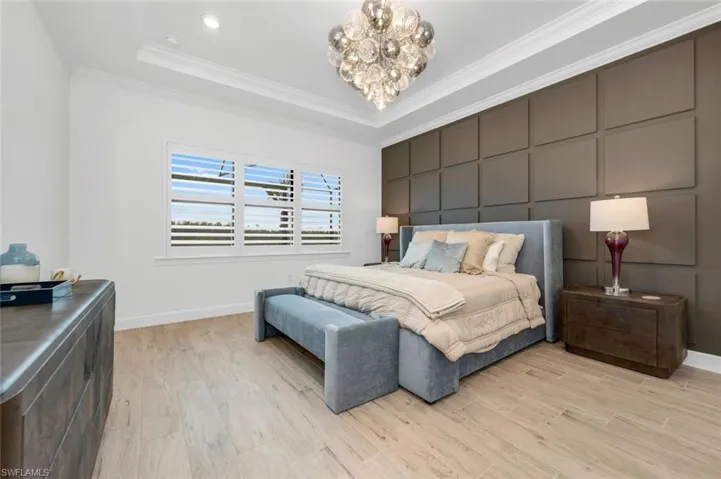 Bedroom with light hardwood / wood-style floors, a notable chandelier, ornamental molding, and a raised ceiling