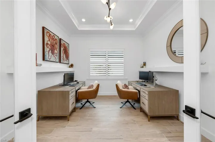 Office area with ornamental molding, light hardwood / wood-style floors, and a raised ceiling