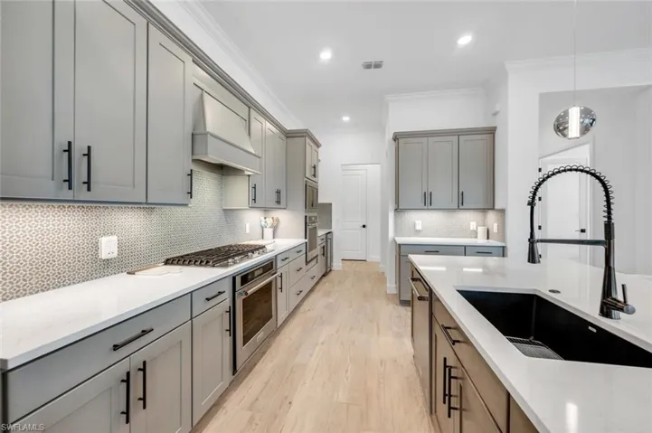Kitchen with custom range hood, sink, crown molding, light wood-type flooring, and appliances with stainless steel finishes