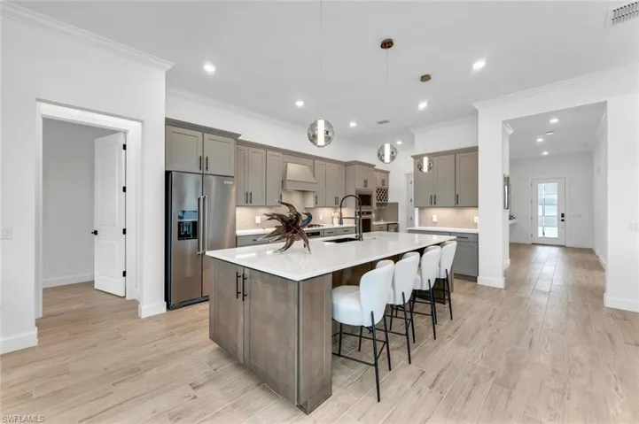 Kitchen with high end refrigerator, hanging light fixtures, a center island with sink, custom exhaust hood, and light hardwood / wood-style floors